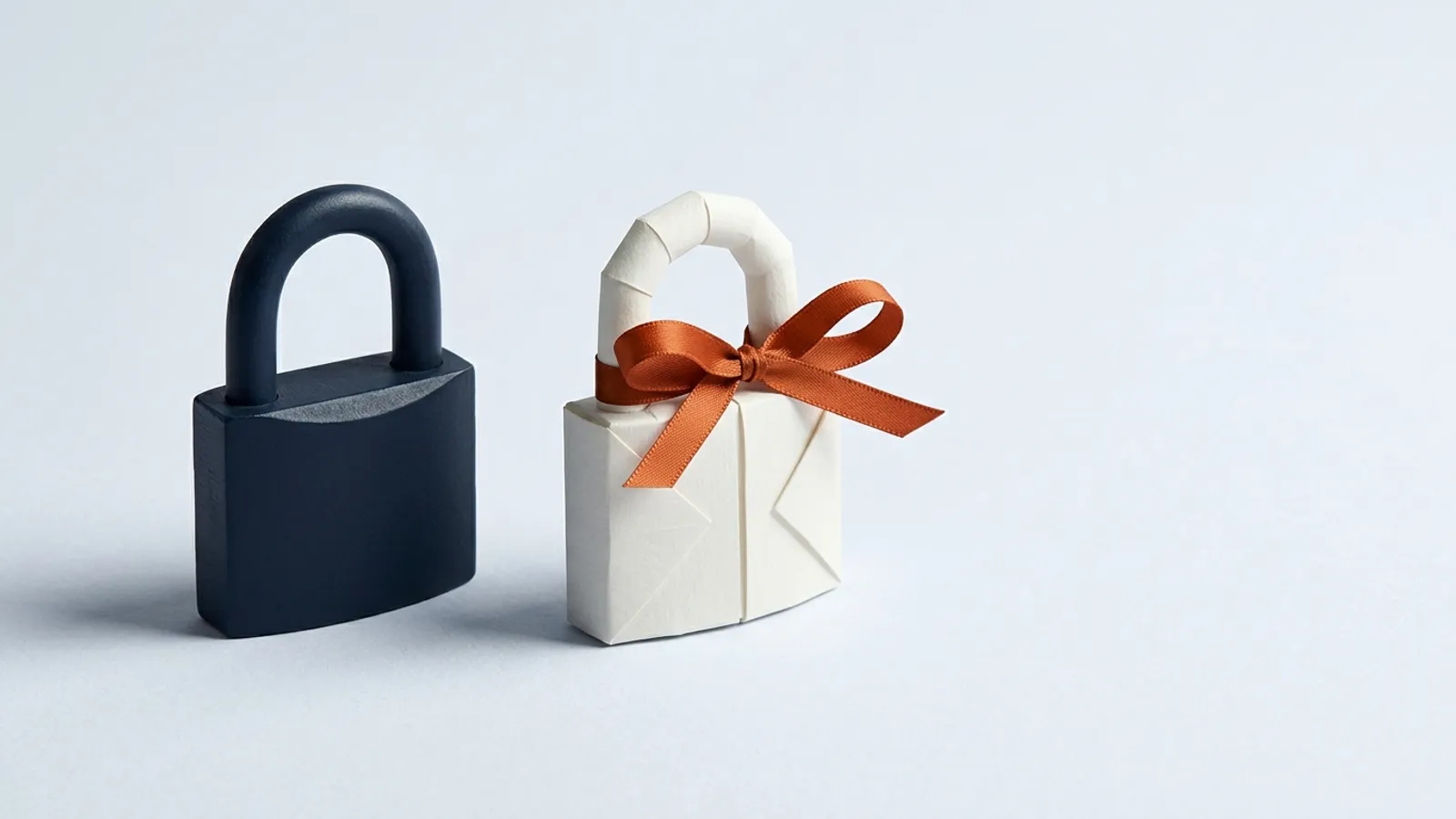 A heavy steel padlock sits next to an identical padlock folded from paper and tied with a ribbon.
