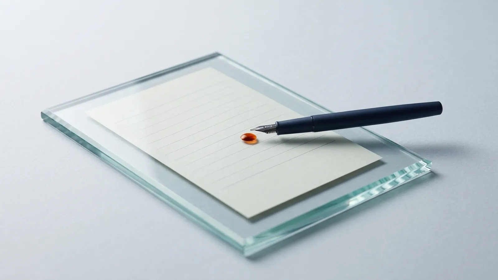 A fountain pen rests on a thick slab of glass, unable to reach the blank paper sealed beneath it.